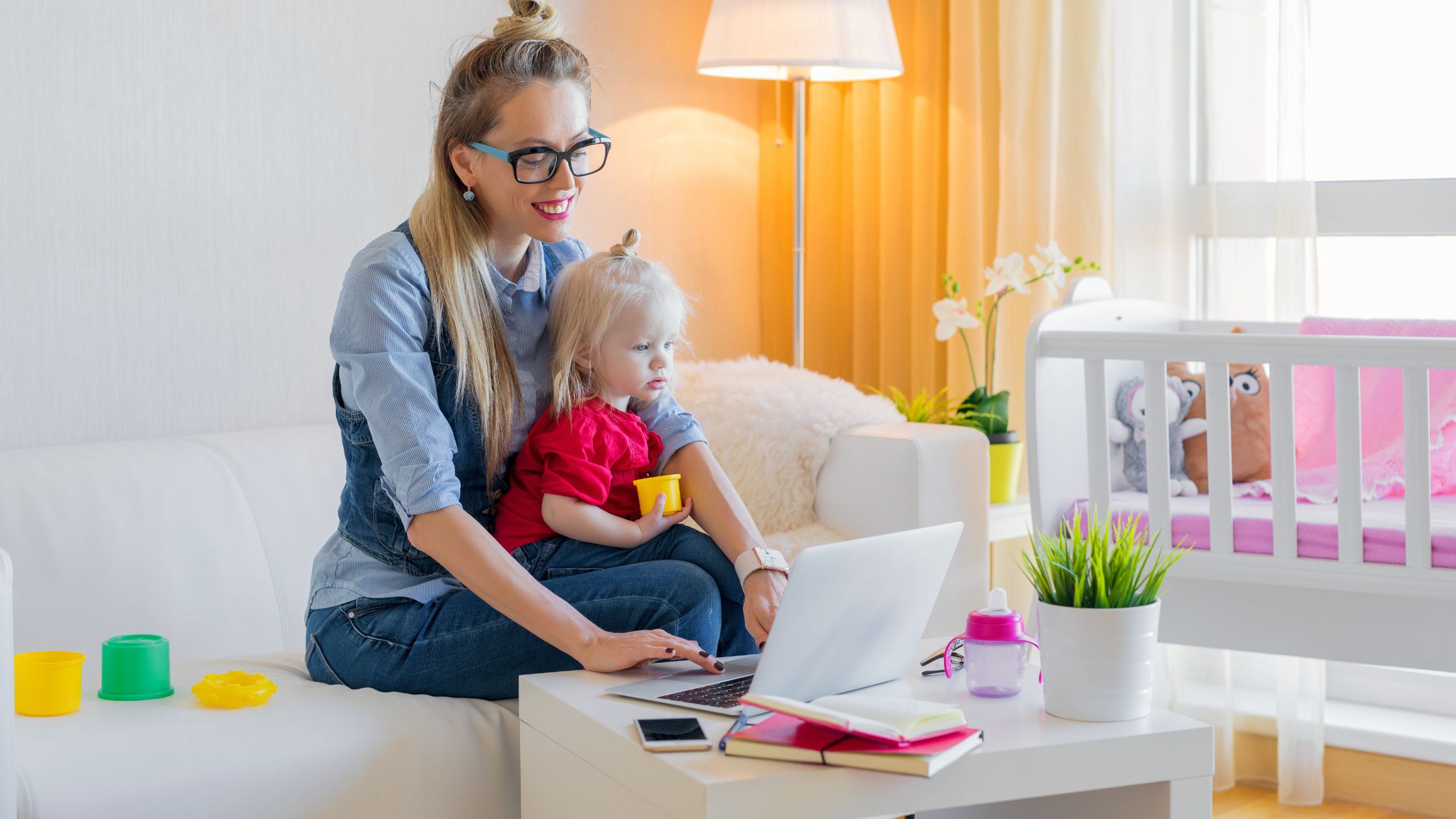 Woman typing on laptop in bedroom with daughter