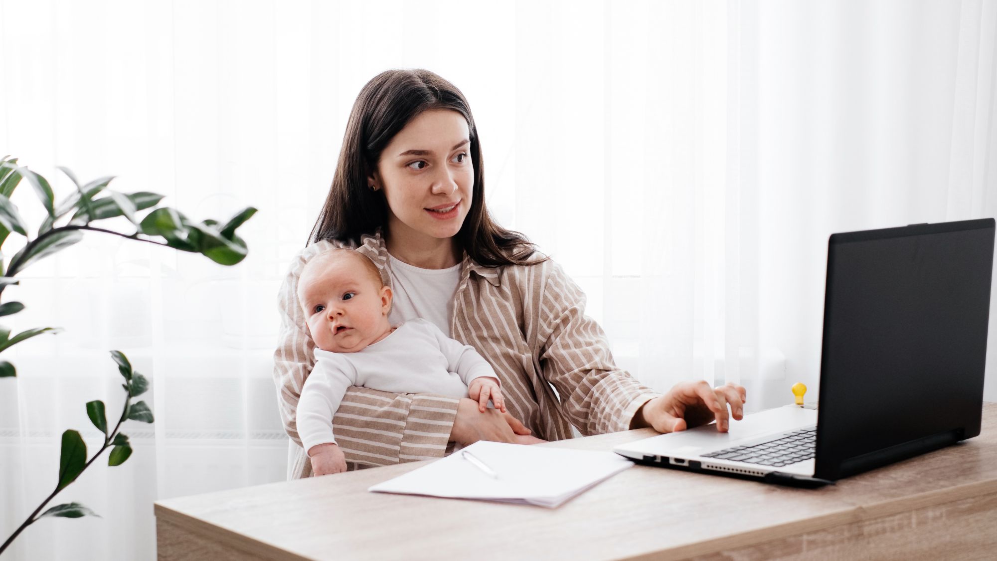 Woman typing on laptop and holding baby